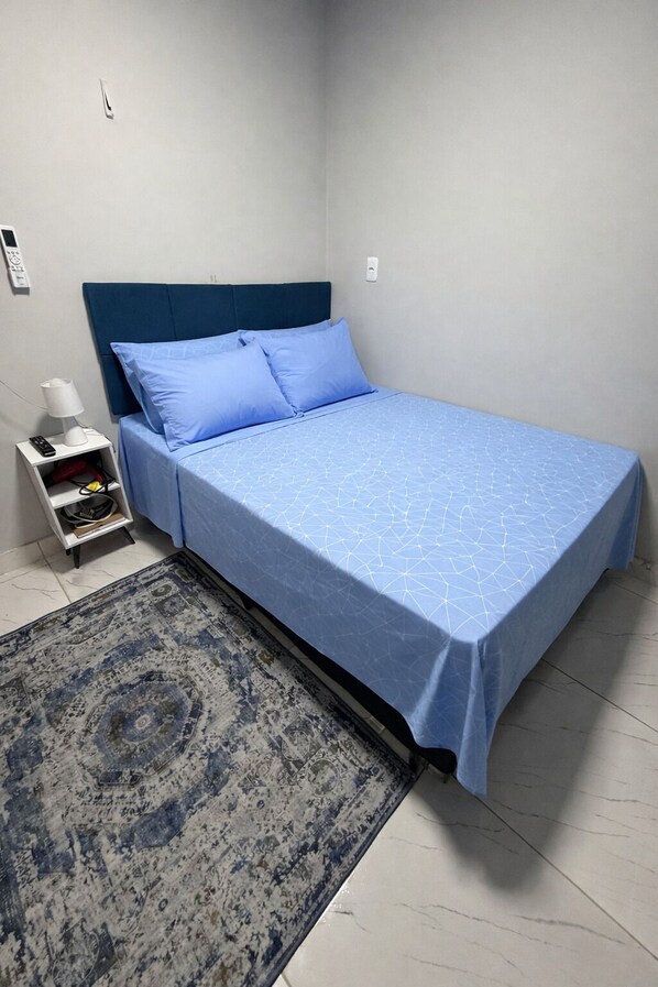 A bedroom with a bed, a nightstand, a lamp, and a patterned rug. - AmazHost - Blue house ideal for couples with Wi-Fi (Belém)