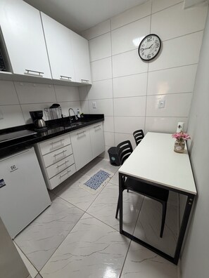 A kitchen with white cabinets, a black countertop, a coffee maker, a sink, a clock, and a table with chairs. - AmazHost - Blue house ideal for couples with Wi-Fi (Belém)
