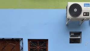A building with a blue wall, a brown door with a decorative metal gate, a window with a wrought iron design, and a tiled lower section. - AmazHost - Blue house ideal for couples with Wi-Fi (Belém)