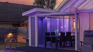A modern outdoor pool area with a covered patio, a poolside table, and chairs. - Skreanäs by Interhome (Falkenberg)