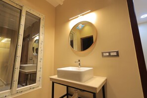 A bathroom with a white sink, a round mirror, and a window with a white frame.