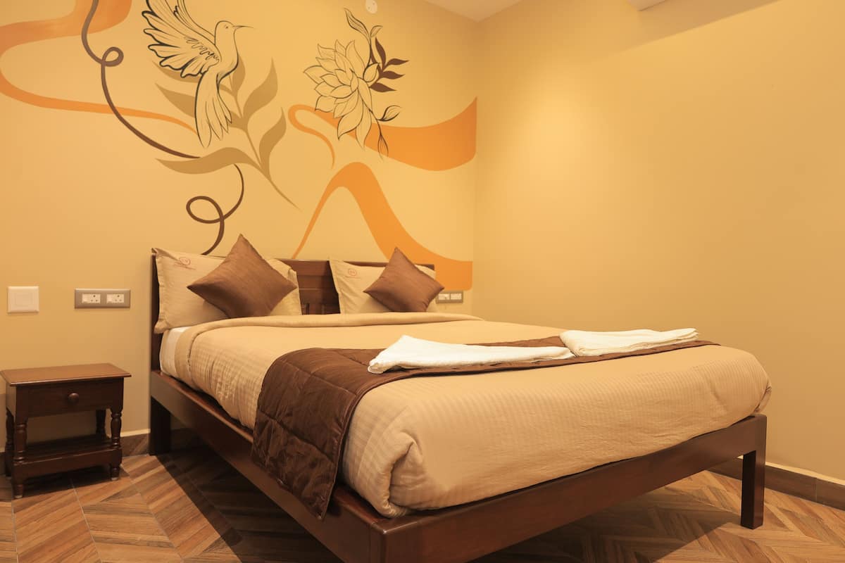 A neatly made bed with a brown headboard, a small bedside table, and a wall with a floral and abstract design.