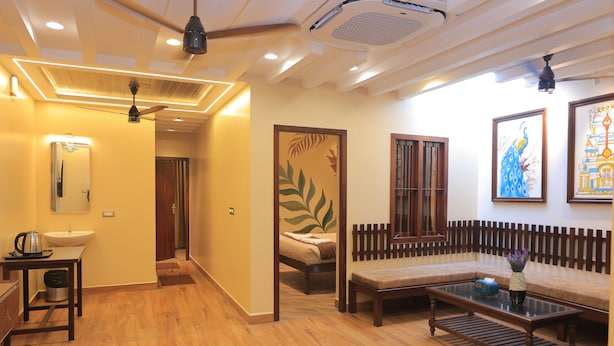 A hotel room with a wooden floor, a sofa, a coffee table, a bed, a mirror, and a ceiling fan. - Sasirekha Residency & Homestay (Puducherry)