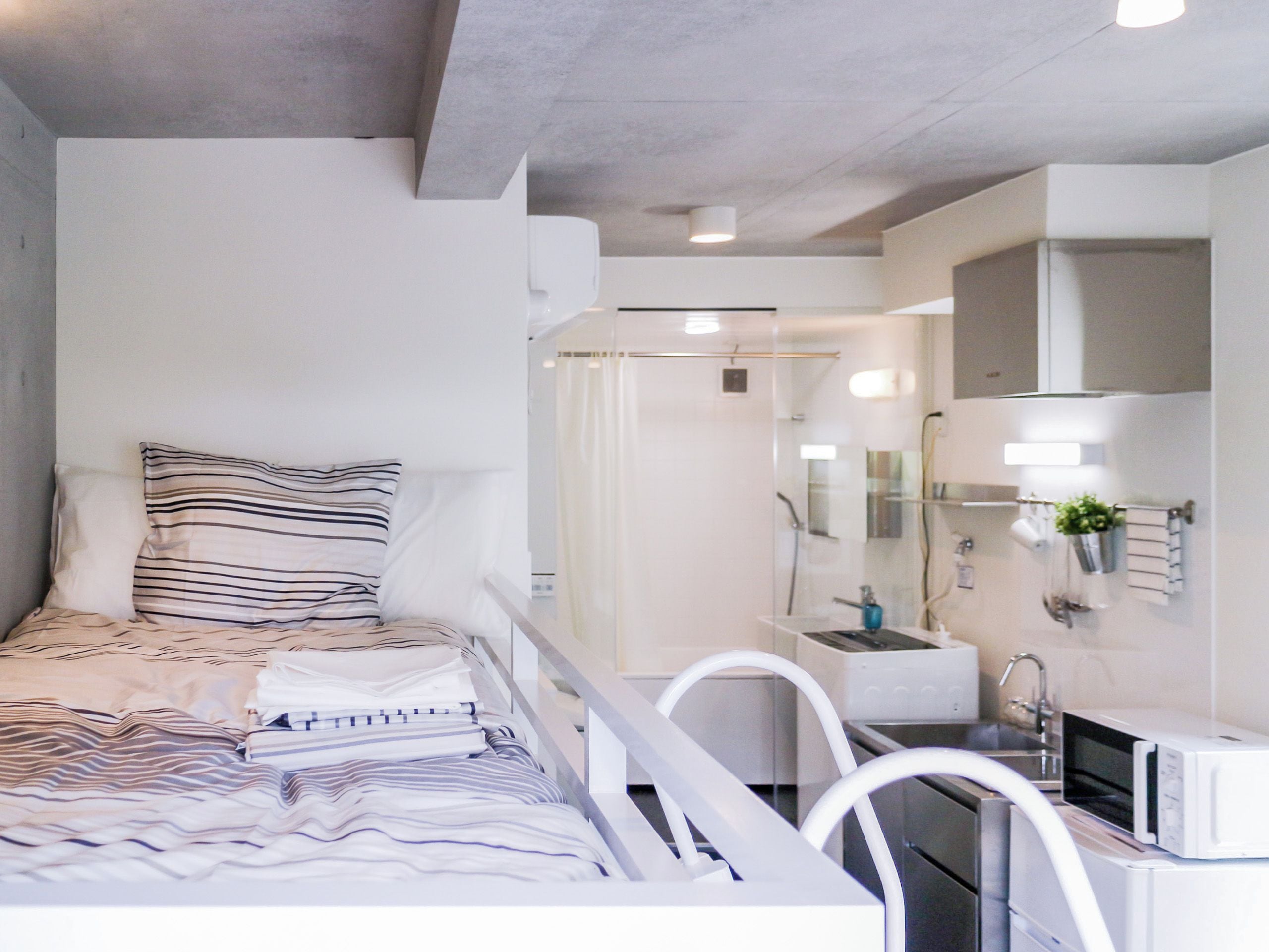 A modern bedroom with a bed, bedside tables, a mirror, and a bathroom with a sink and shower.