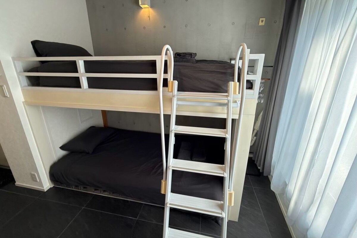 A bunk bed room with a ladder, a wall-mounted light, and a curtain.