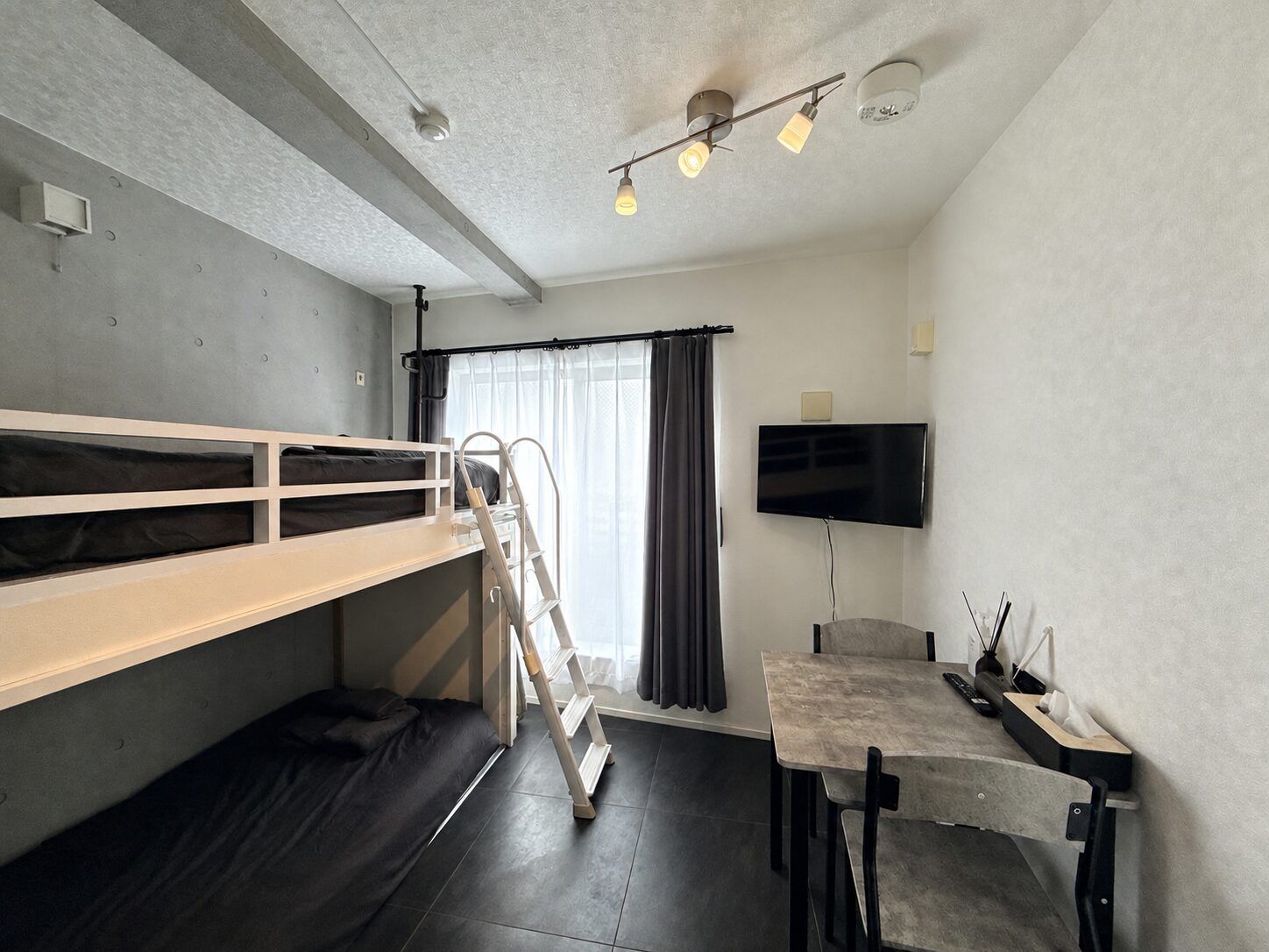 A compact room with bunk beds, a desk, a chair, a television, and a window with curtains.
