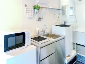 A modern kitchen with a built-in microwave, stainless steel sink, and a glass shower enclosure. - URBANAGE Takadanobaba (Tokyo)