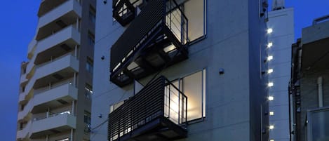 A modern multi-story building with a flat facade, balconies, and a ground entrance.