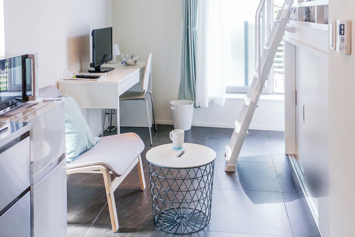 A modern hotel room with a desk, chair, and a round table with a coffee cup.