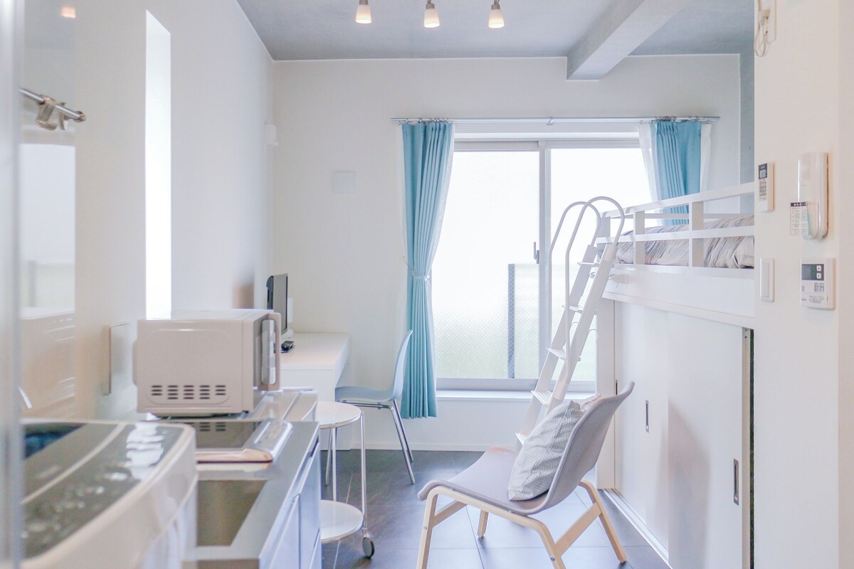 A modern, well-lit room with a bed, bedside table, and a window with curtains.