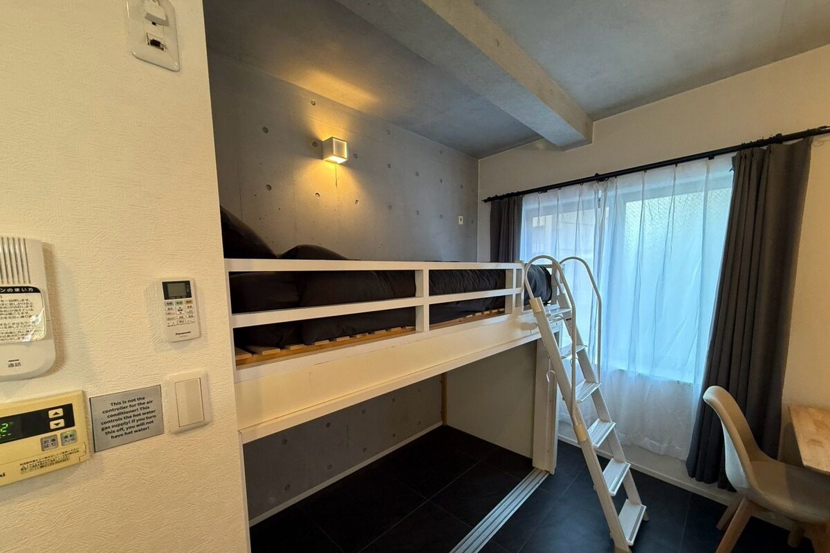 A bunk bed room with a ladder, a thermostat, and a window with curtains.