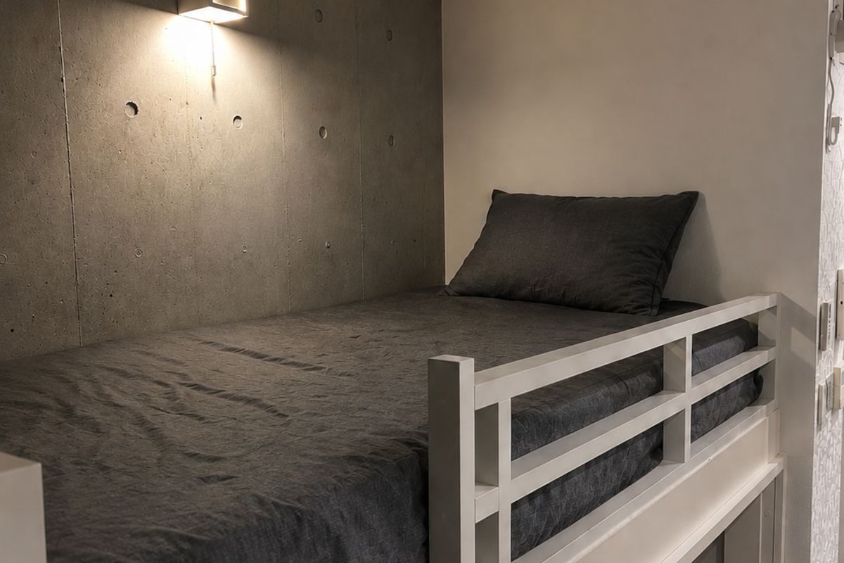 A bunk bed with a headboard, a bedside table, and a wall-mounted light fixture.