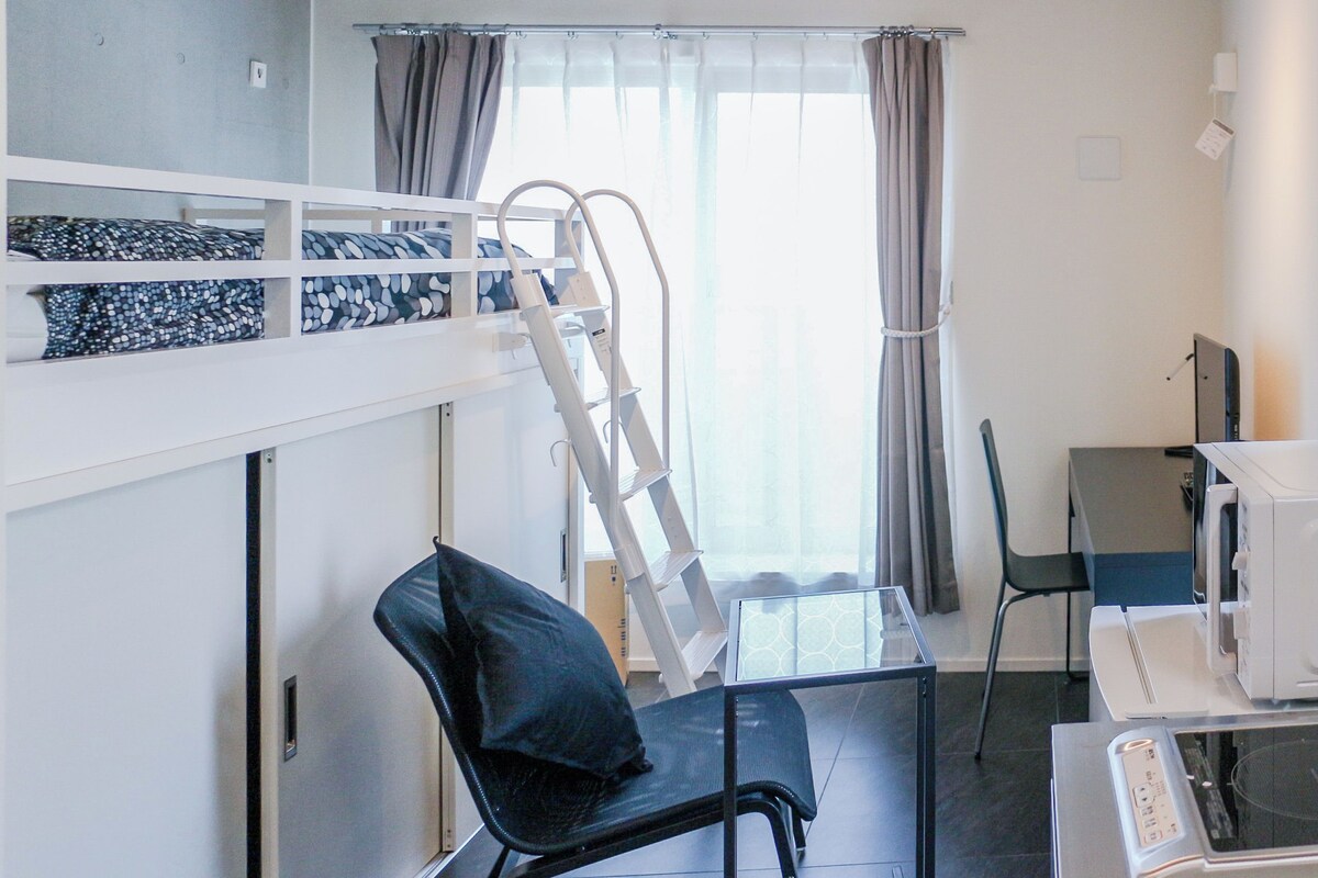 A room with a bunk bed, a desk with a computer, a chair, and a microwave.