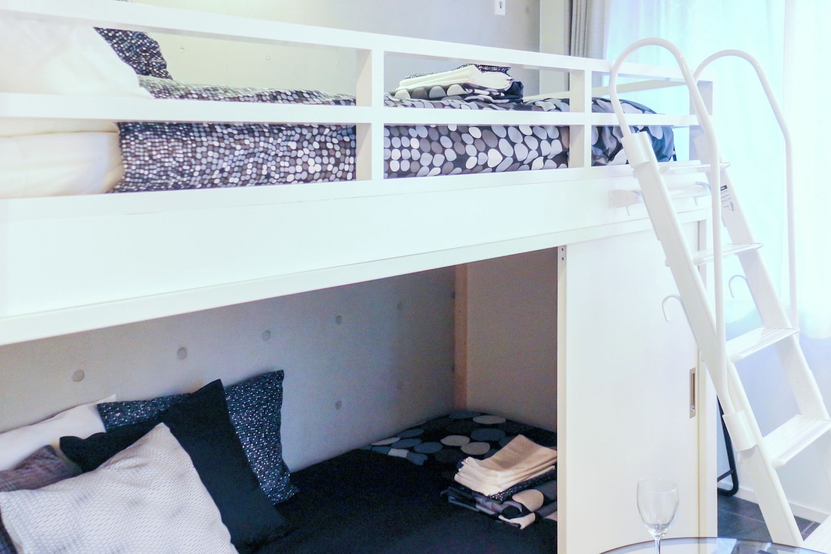 A bunk bed with a ladder, a small seating area with cushions, and a glass table with a wine glass.