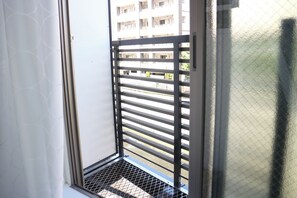 A window with a metal grill and a view of a building with multiple balconies. - URBANAGE Takadanobaba (Tokyo)