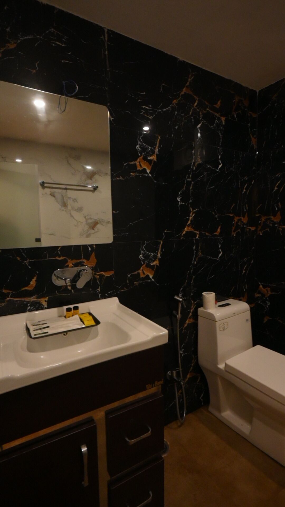 A bathroom with a black marble wall, a white sink, and a toilet.