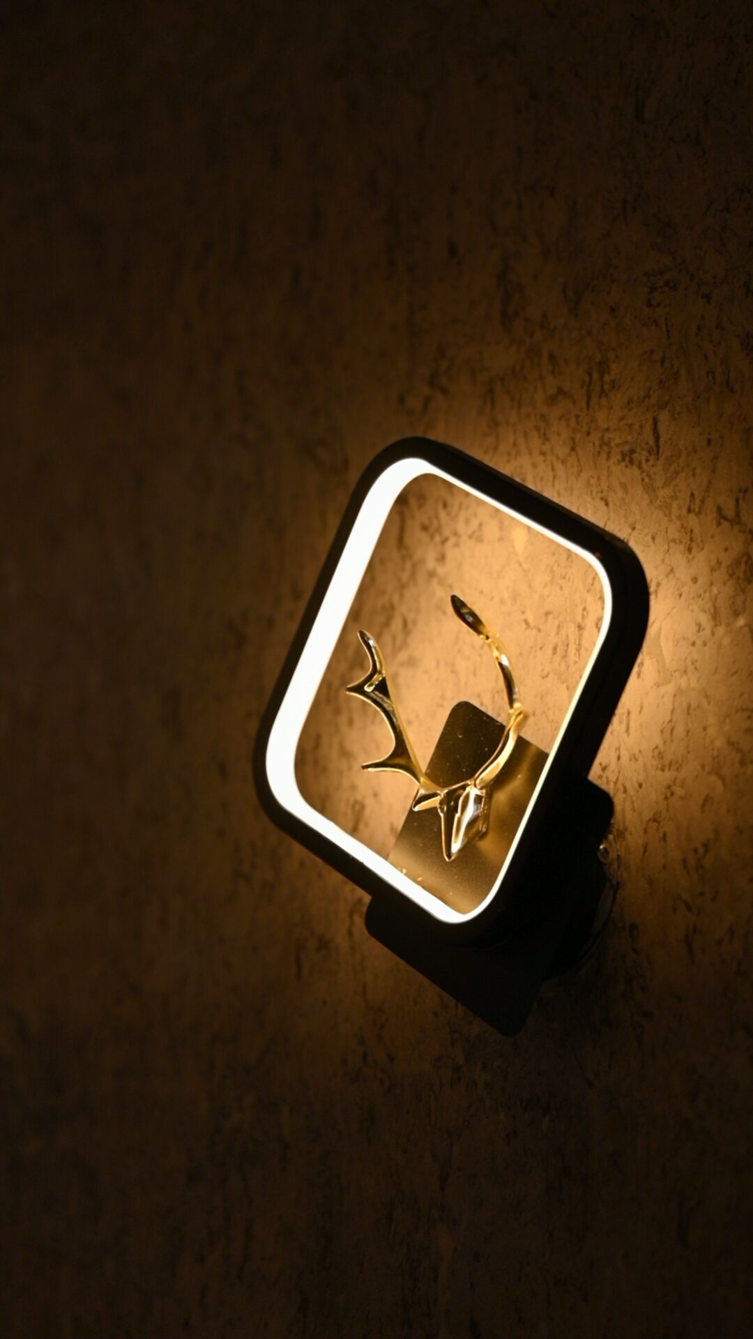 A square-shaped, illuminated object with a reflective surface, possibly a decorative item or a piece of furniture, on a textured surface.