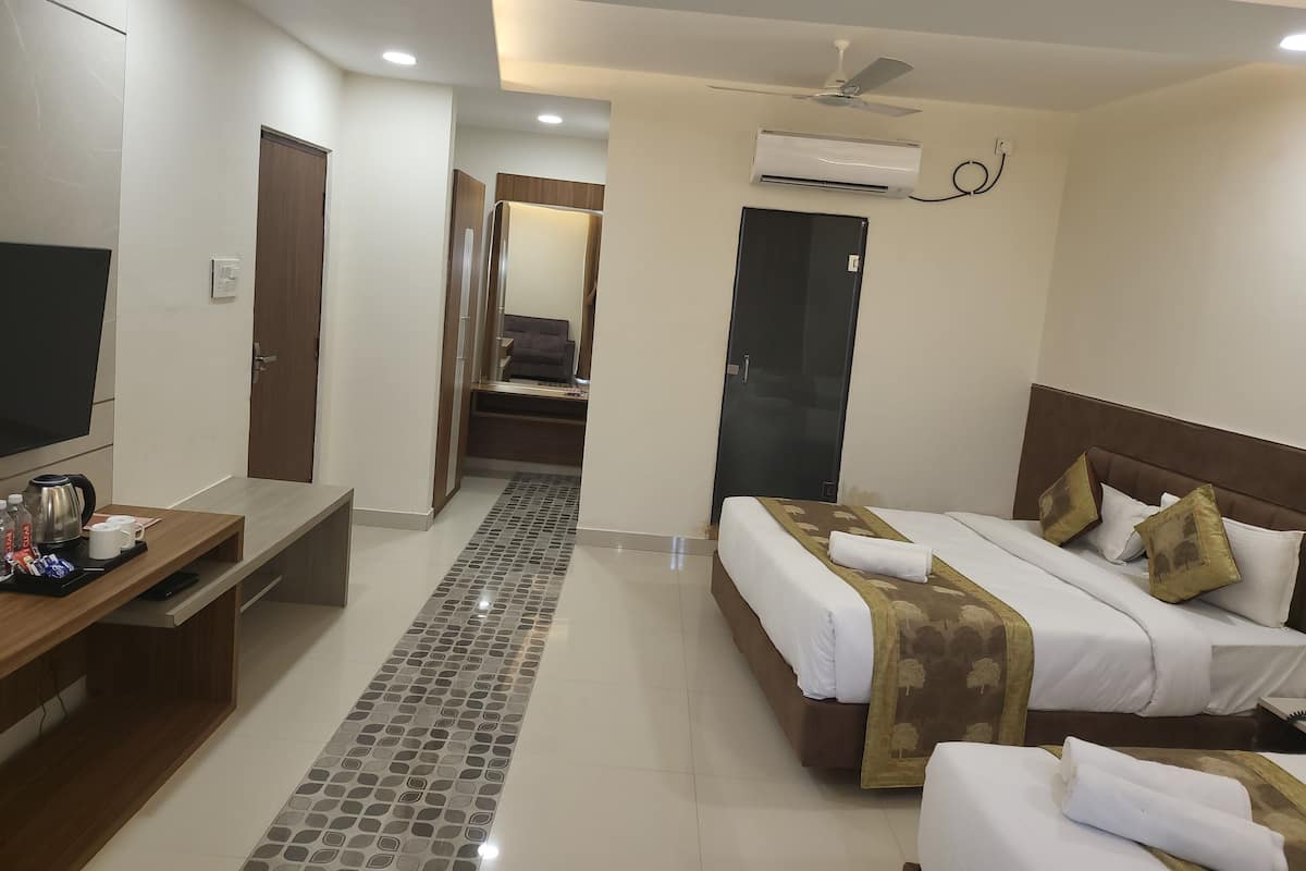 A hotel room with a bed, bedside table, TV, and a hallway leading to a bathroom.