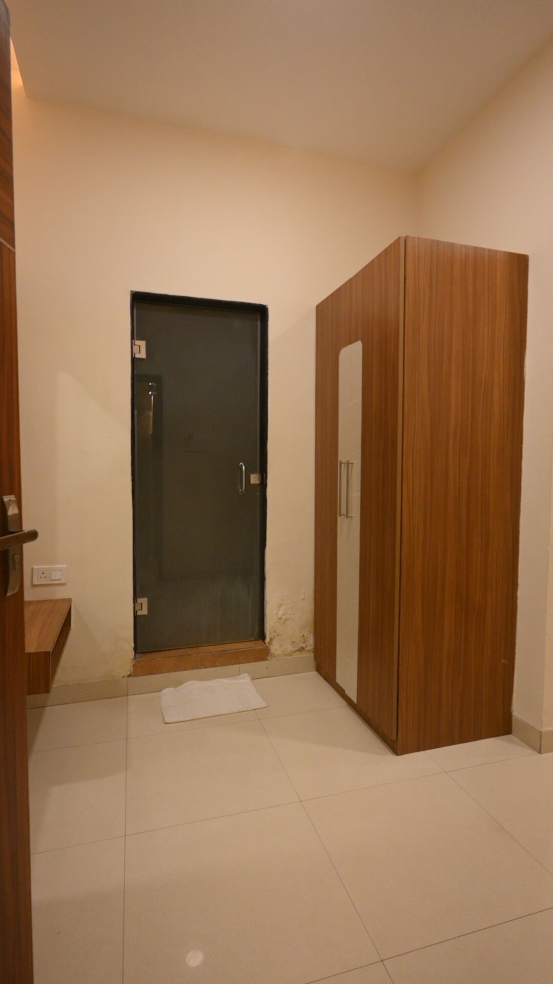 A room with a dark door, a wooden wardrobe, and a small white mat on the floor.