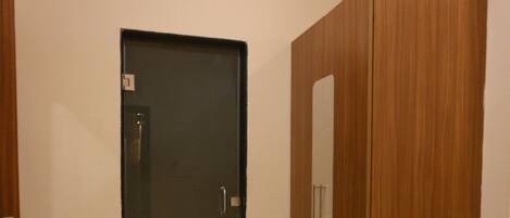 A room with a dark door, a wooden wardrobe, and a small white mat on the floor.