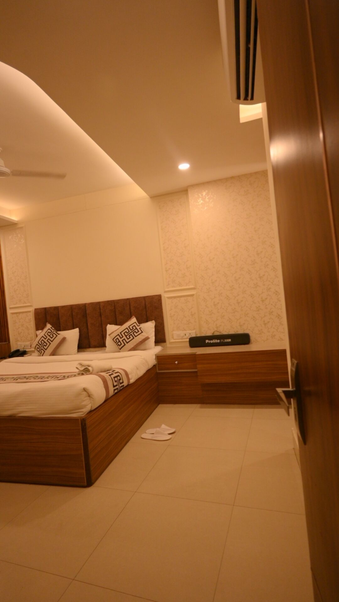 Un dormitorio con una cama, una mesita de noche, un dispositivo Prolite Plus 5000 y una puerta.