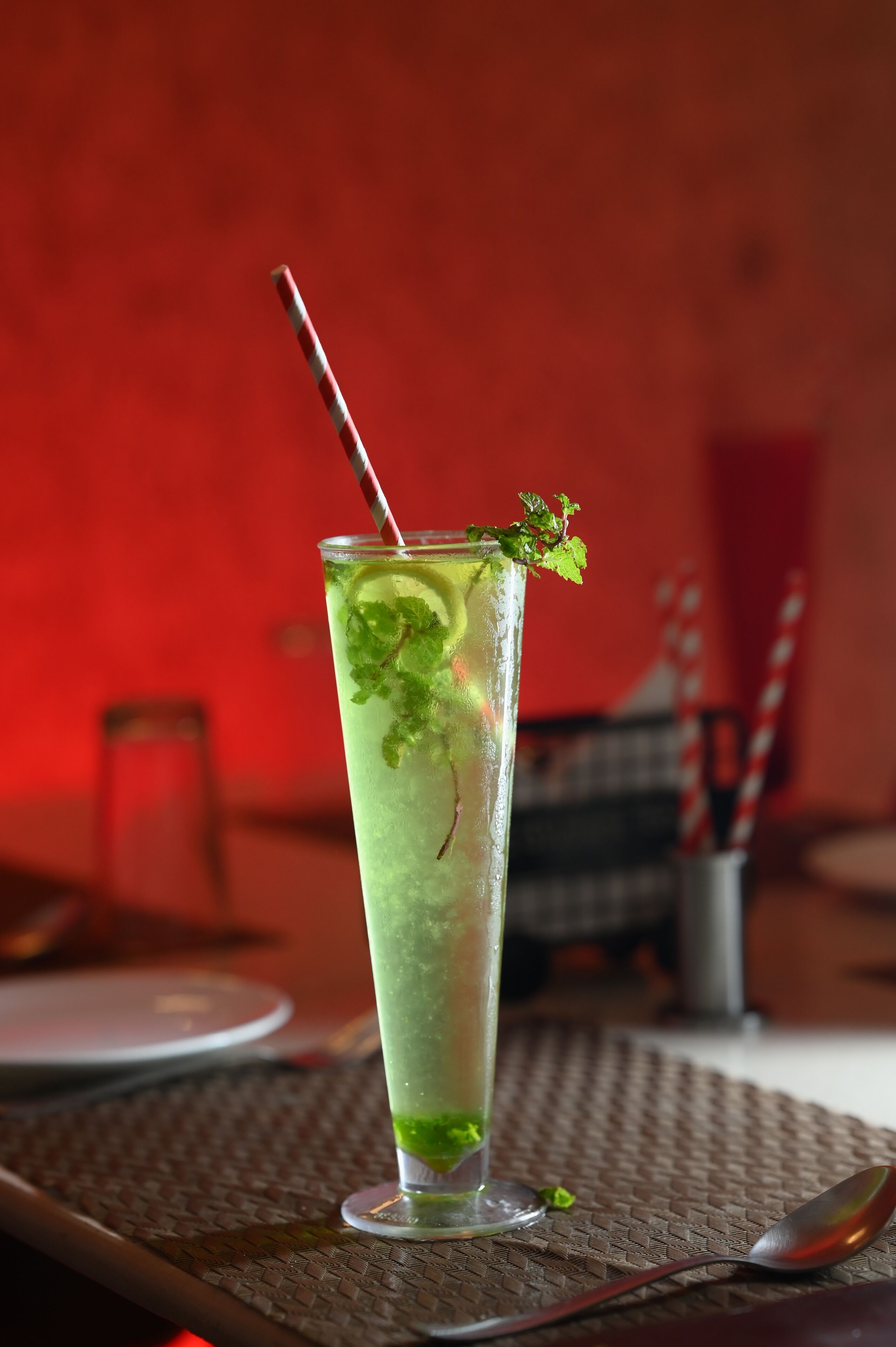 A tall glass with a striped straw and mint garnish, placed on a woven placemat.