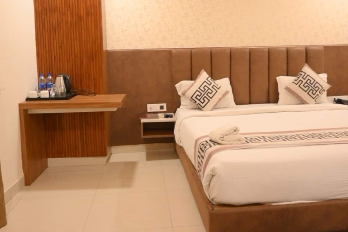 A modern hotel room with a large bed, wooden headboard, and a small bedside table with a kettle and water bottles.