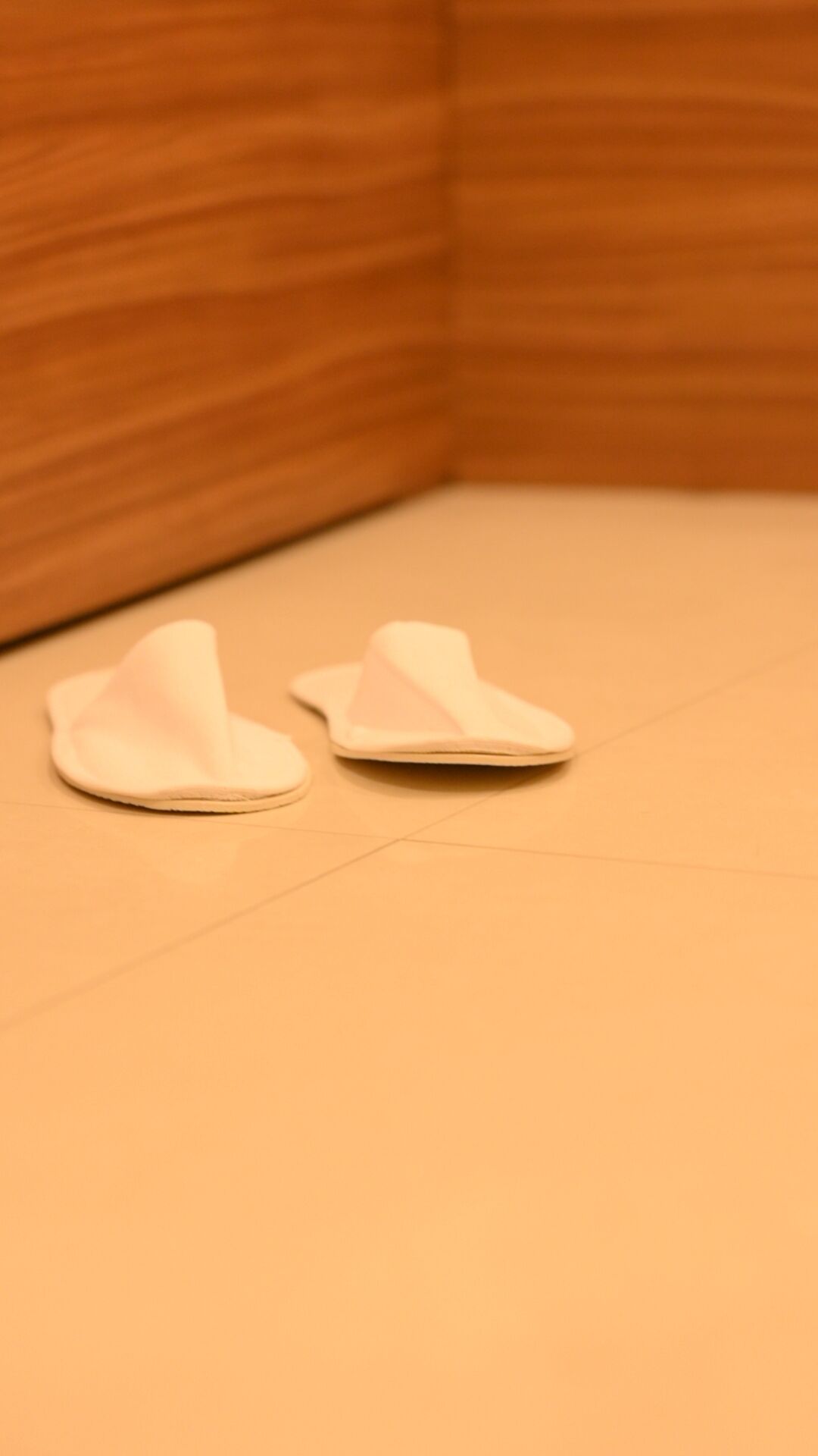 Une paire de pantoufles blanches sur un sol beige, dans une pièce aux murs recouverts de lambris en bois.
