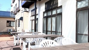 Des tables en bois et des chaises en plastique blanc sont disposées sur une terrasse.