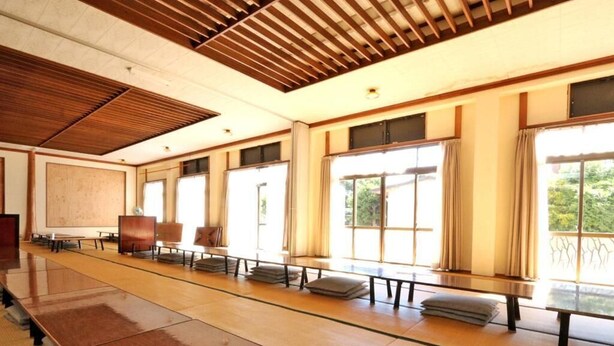 Une salle de conférence dotée de longues tables, de grandes fenêtres et d’un plafond en bois.