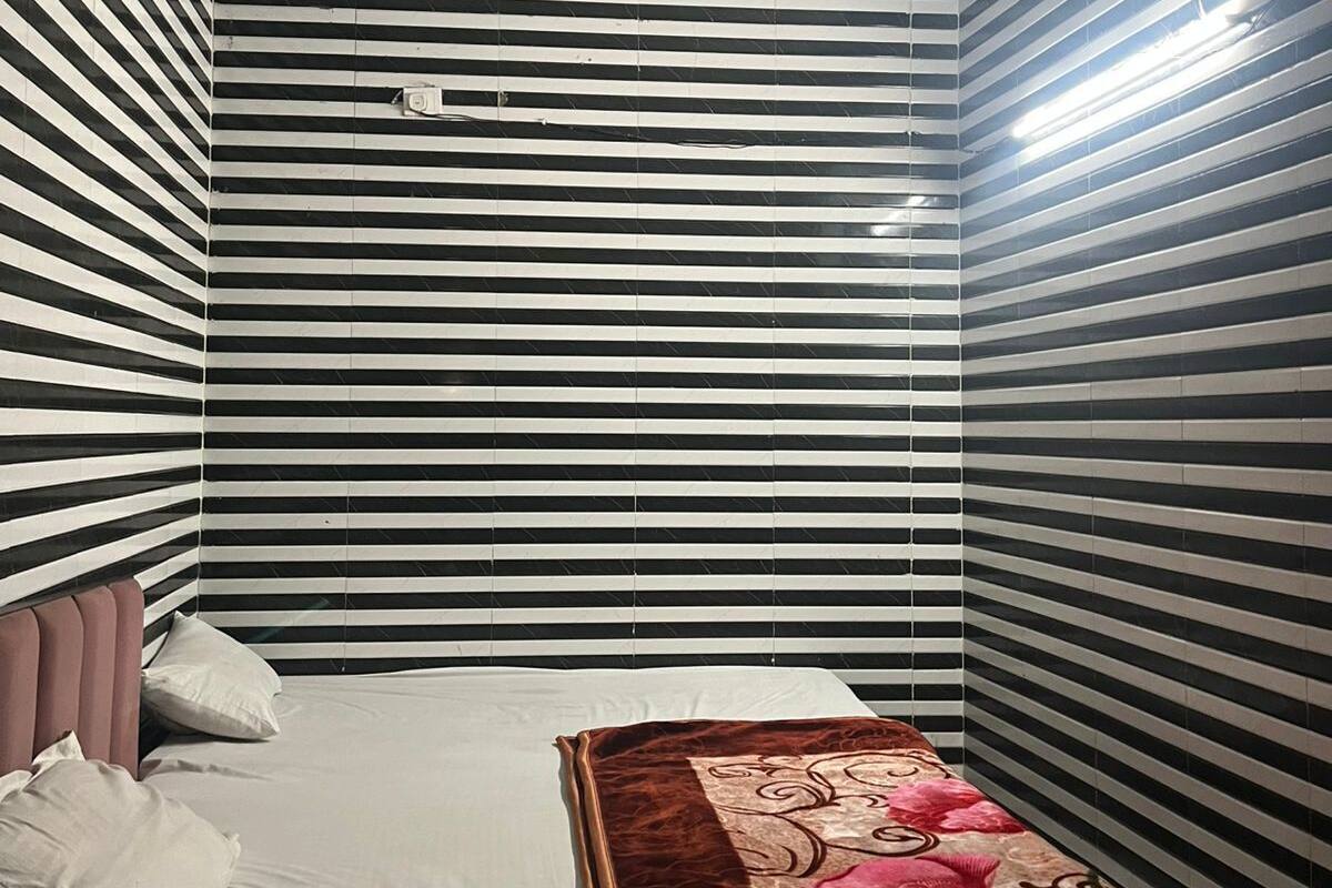 Une pièce aux murs rayés, un lit recouvert d’une courtepointe à motifs floraux, un ventilateur de plafond et une petite table.