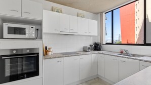 A modern kitchen with white cabinets, a microwave, a stove, and a toaster. - Tasman Towers Unit 8 (Port Macquarie)