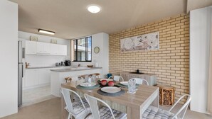 A modern kitchen with white cabinets, a wooden island, and a brick accent wall. - Tasman Towers Unit 8 (Port Macquarie)