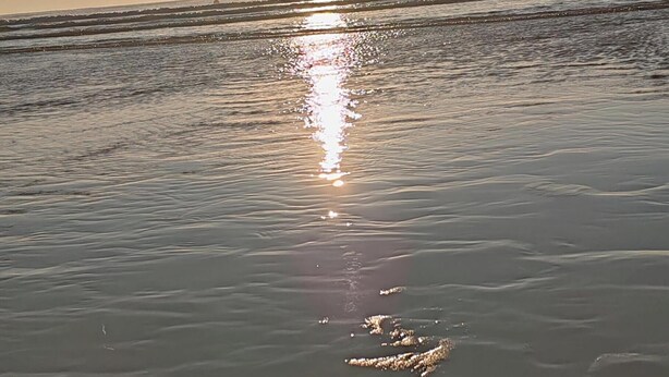 Ein Strand, auf dem sich die Sonne im Wasser spiegelt.