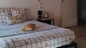 Ein Schlafzimmer mit Holzboden, einem Bett mit gemusterten Betttextilien, einem Nachttisch mit Lampe und einer Tür.