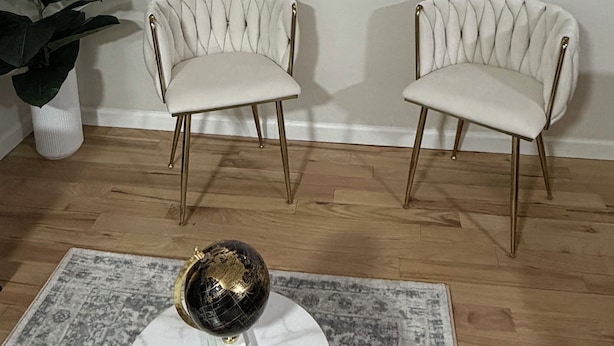 Una habitación con dos sillones tapizados con patas doradas, un adorno circular en la pared y dos lámparas de pared.