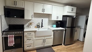 Una cocina moderna con armarios blancos, electrodomésticos de acero inoxidable y un backsplash de baldosas en patrón de espiga.