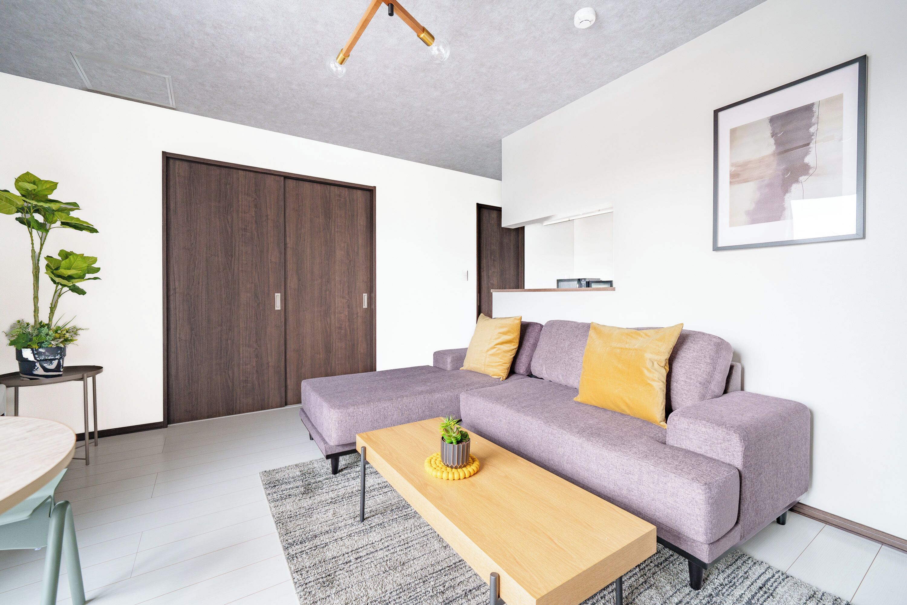 A modern living room with a sectional sofa, a wooden coffee table, a potted plant, and a large framed artwork on the wall.