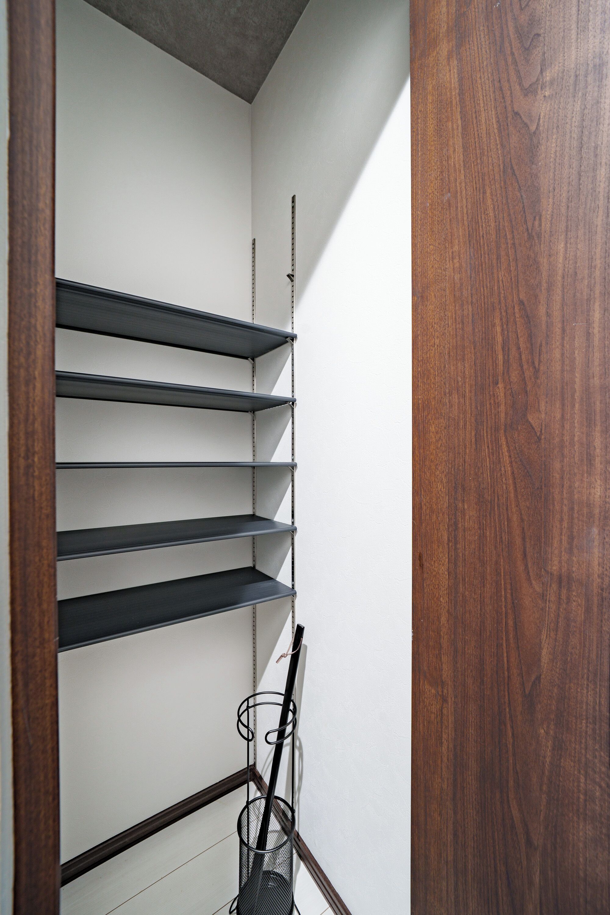 Esquina de una habitación con un marco de madera, pared blanca y una estantería metálica.