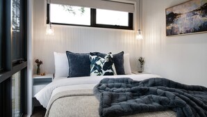 Een slaapkamer met een bed, twee nachtkastjes, een raam en een schilderij aan de muur.
