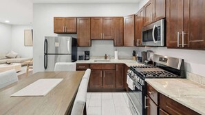 A modern kitchen with wooden cabinets, stainless steel appliances, and a marble countertop. - Modern Apartment w/ Parking & Fast NYC PATH Access (Jersey City)