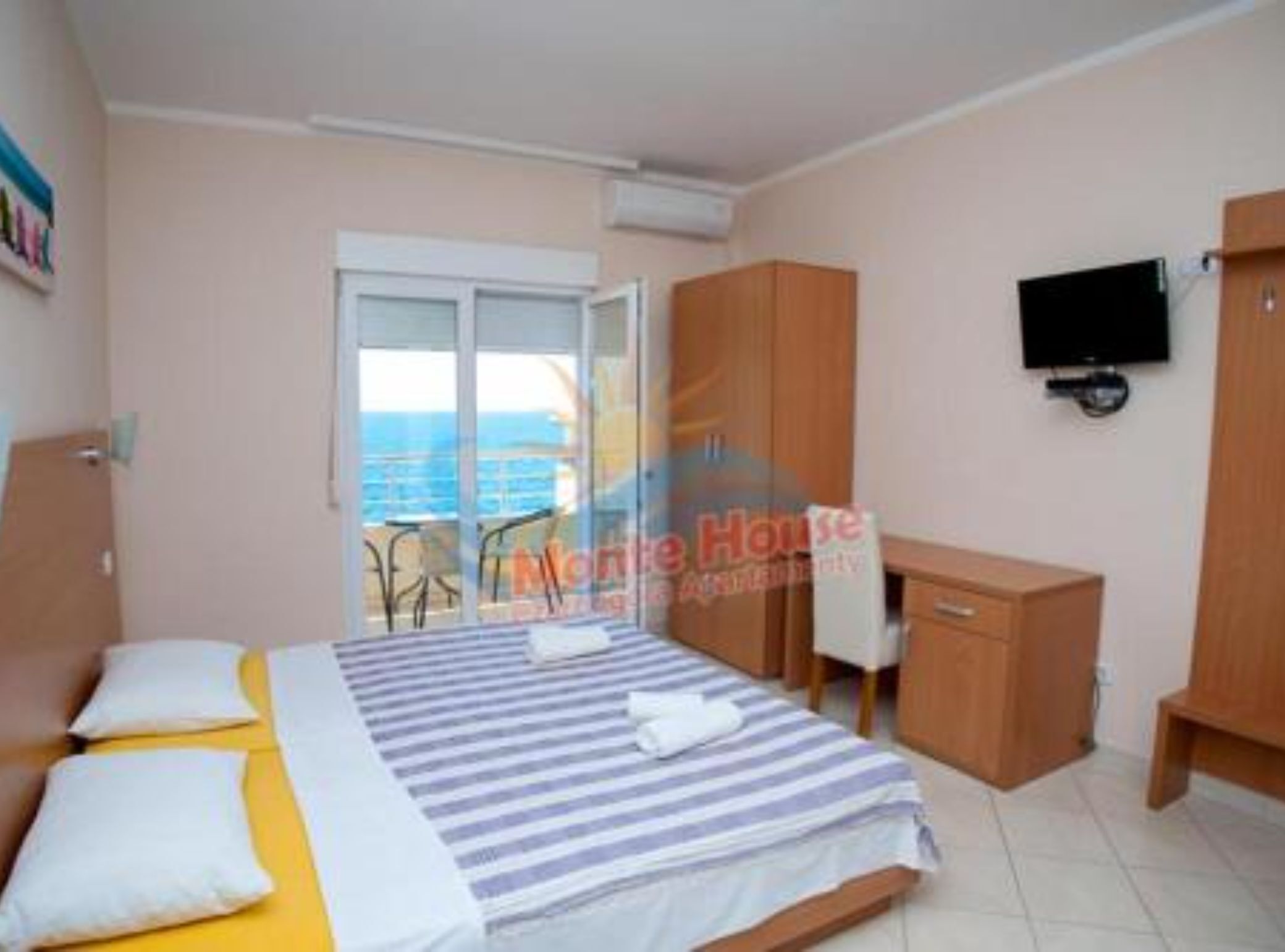 A bedroom with a bed, a TV, a wardrobe, and a window with a view of the sea.