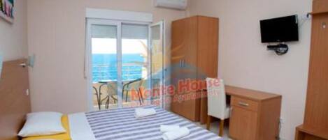 A bedroom with a bed, a TV, a wardrobe, and a window with a view of the sea.