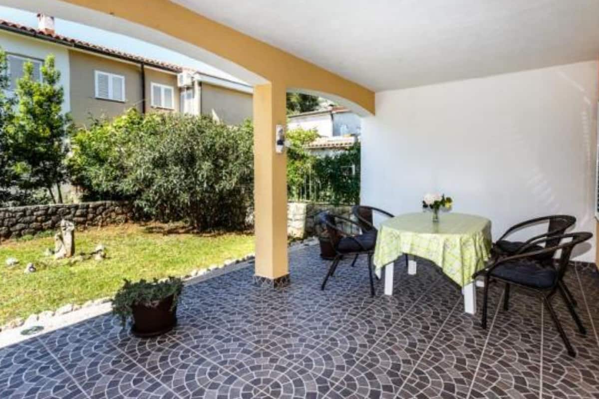 Un patio techado con piso de baldosas, una mesa redonda con sillas y una planta en maceta.