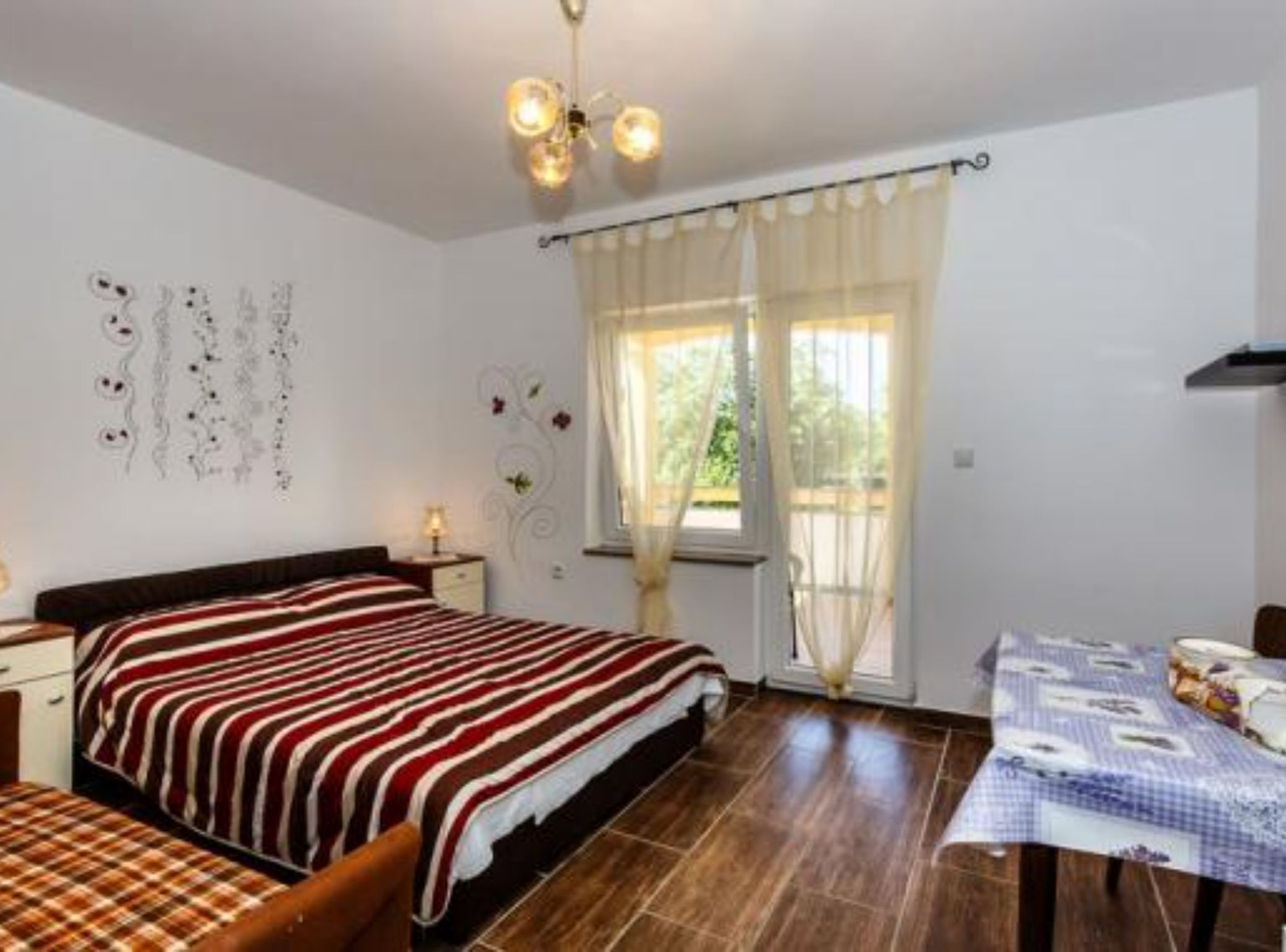 A bedroom with a bed, bedside table, lamp, window with curtains, and a wall decoration.