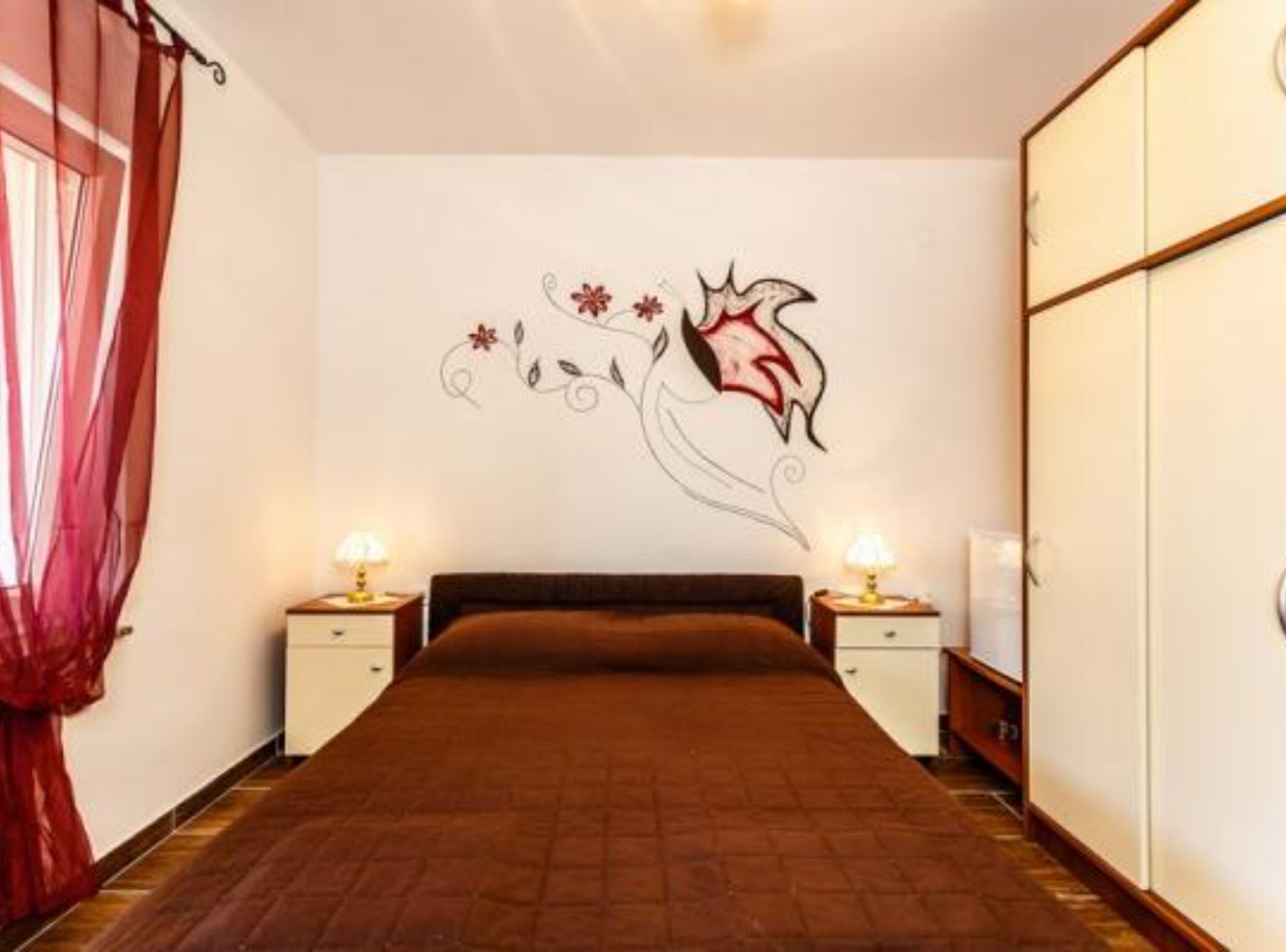 Een slaapkamer met een bed, twee nachtkastjes met lampen, een wand met bloemendecoratie, en een garderobe.