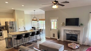 A modern living room with a fireplace, a TV, and a dining area with a kitchen in the background. - 3BR w/ Pool Table & Ping Pong - Near Snowden District, Landers Cnt & Outlet Mall (Southaven)