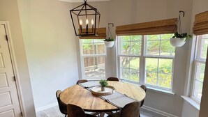 A dining area with a round wooden table, six chairs, a hanging light fixture, and large windows with blinds. - 3BR w/ Pool Table & Ping Pong - Near Snowden District, Landers Cnt & Outlet Mall (Southaven)