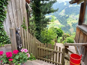 Eine Holztreppe führt zu einem Balkon mit Blick auf ein Tal, ein Holzzaun und eine dekorative Katzenstatue.