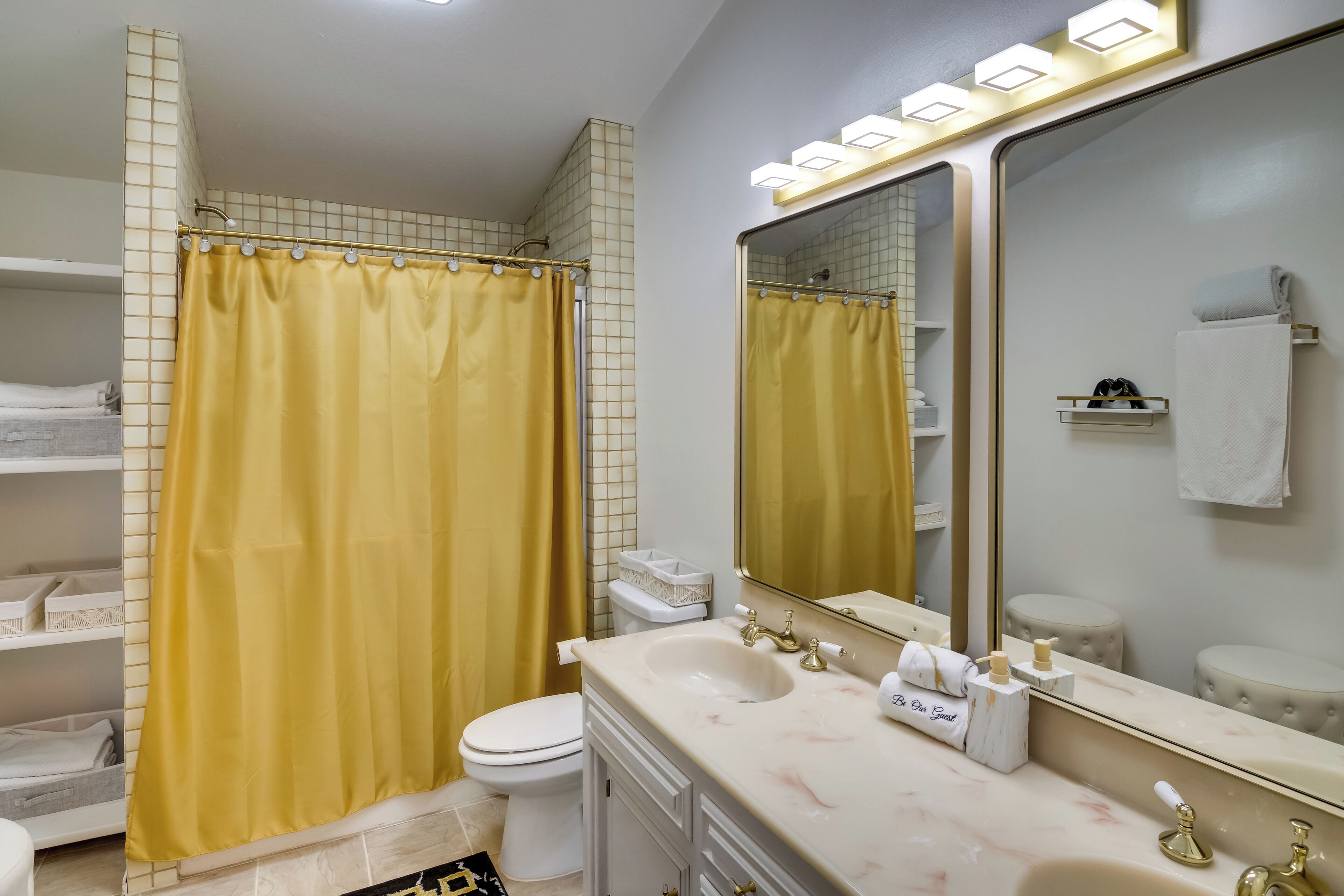 A bathroom with a yellow shower curtain, a white toilet, a marble sink, and a large mirror.